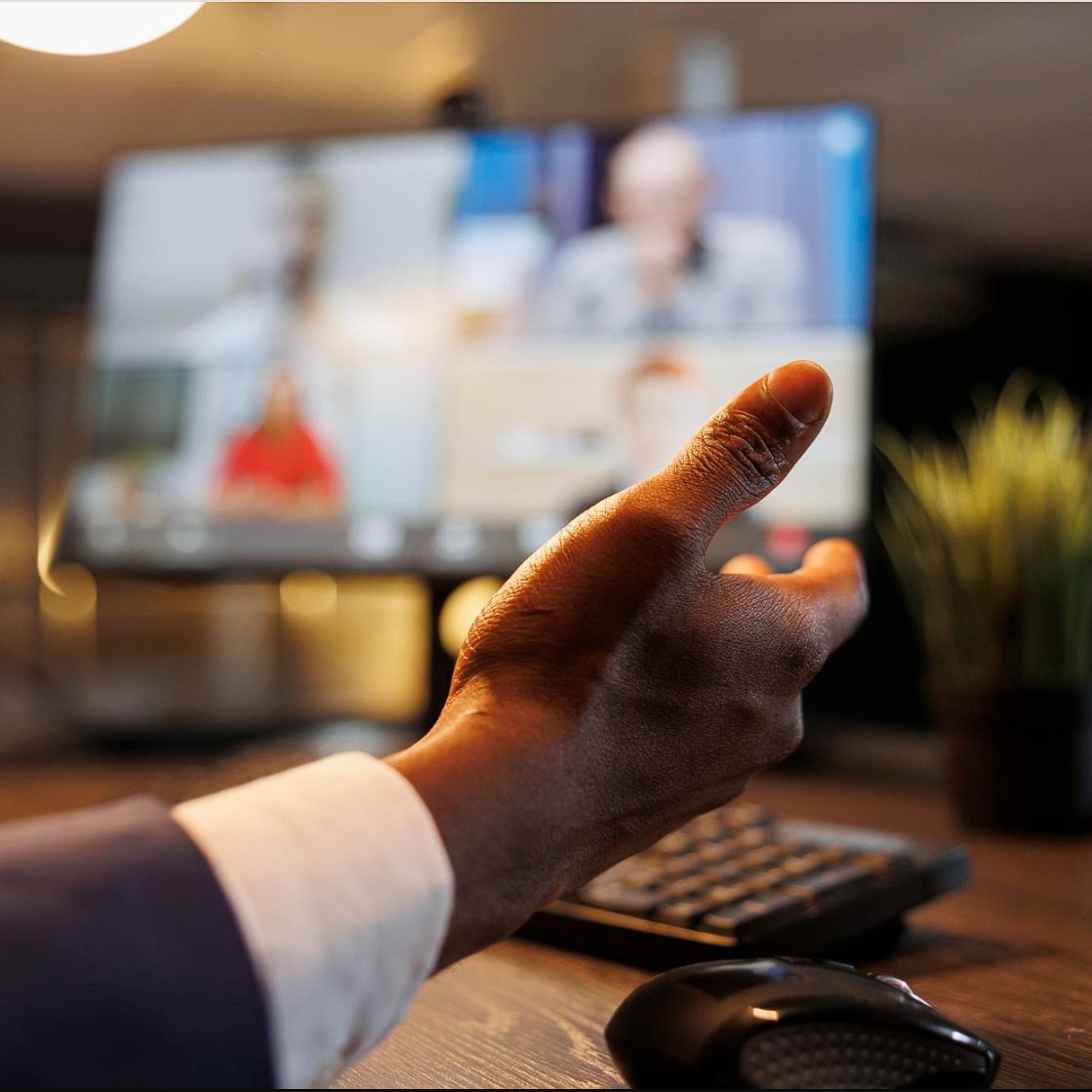 A hand gesturing during a video consultation on a desk monitor